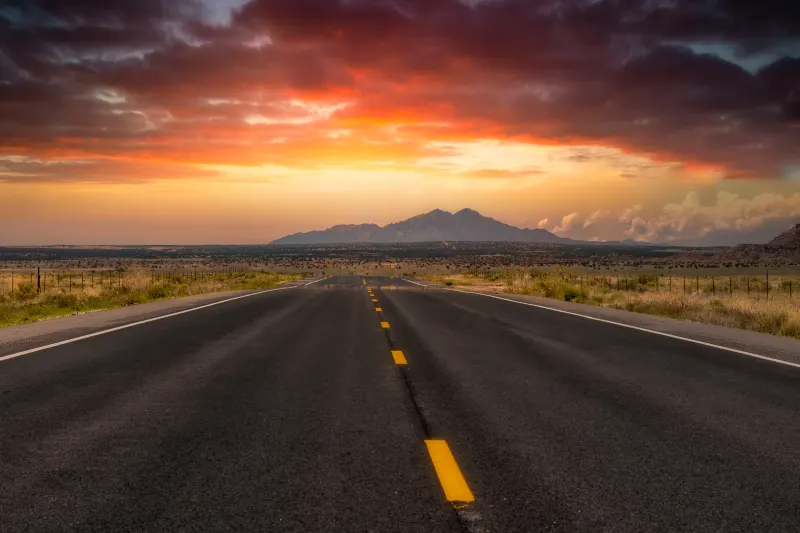 An empty desert highway running toward the mountains at sunset